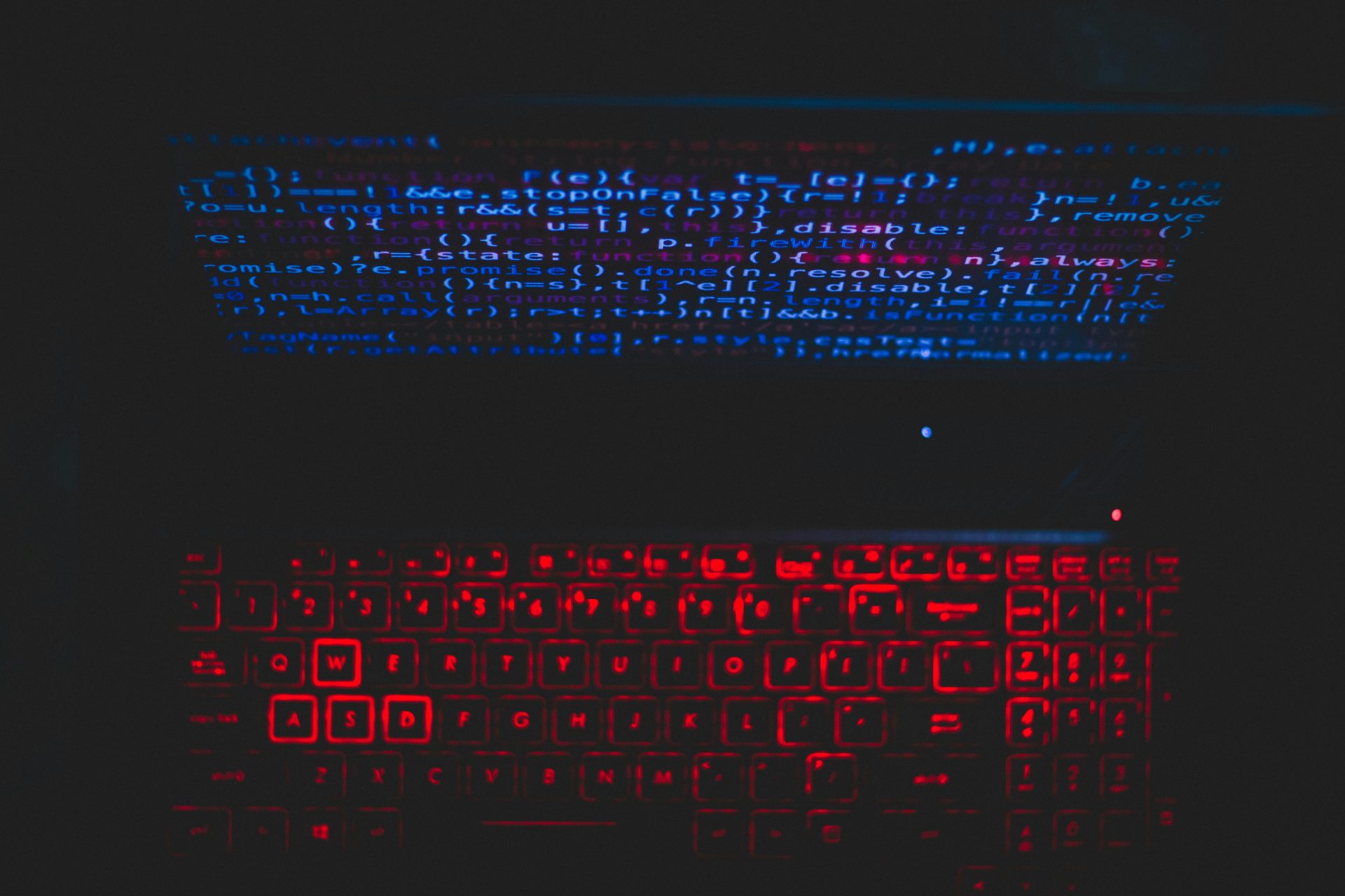 Dark-themed laptop setup with a red glowing keyboard and code on screen, ideal for tech enthusiasts.